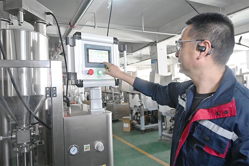 A technician is operating the control panel of a tube filling and sealing machine.